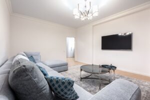 Salon z szarą sofą, szklaną ławą i dywanem, telewizor na ścianie