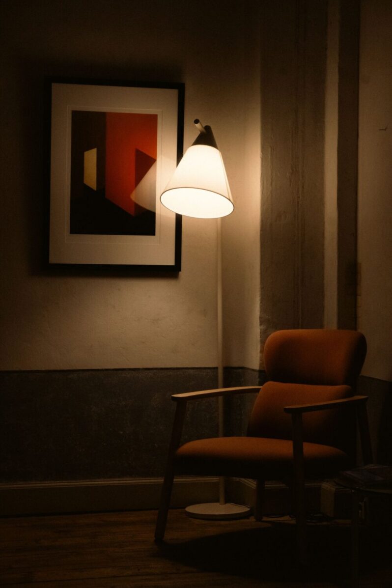 Lampa podłogowa z białym kloszem obok fotela w kąciku do czytania